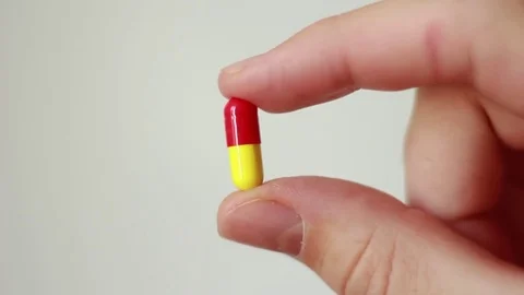 Holding one yellow-red pill in fingers Stock Footage 79589746