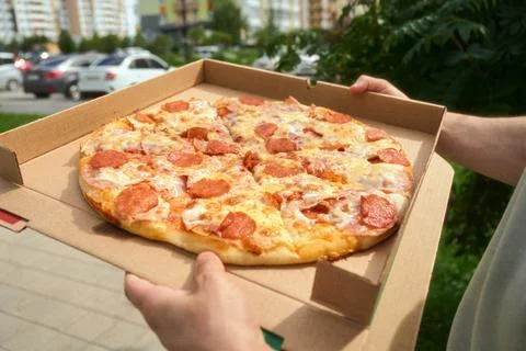 Holding open pizza box on border of grass and urban city street Stock Photos