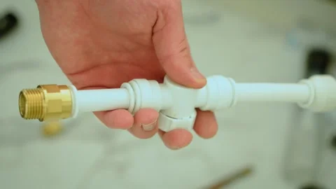 Holding plastic pipe with brass adapter in hand, plumbing components ready for Stock Footage 336309714