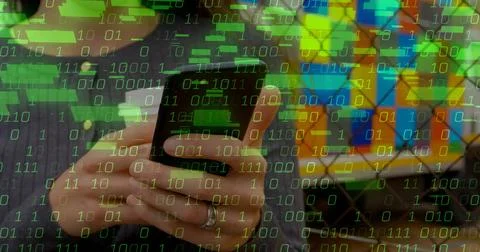 Holding smartphone with ringed left hand at office workspace, showing binary  Foto stock
