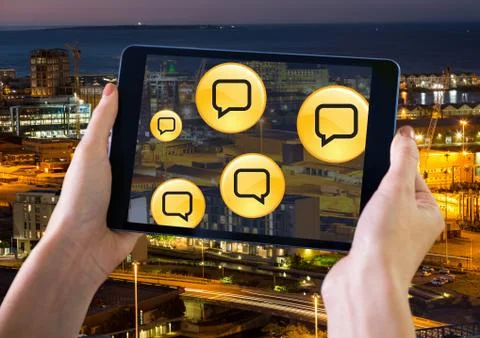 Holding tablet and Chat bubbles over night city Foto stock