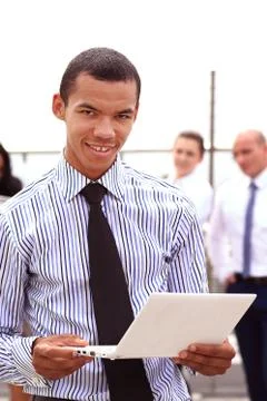 Holding a tablet computer, a young handsome black businessman is standing Stock Photos