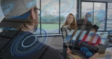 Holding tablet showing AR 3D car, man wearing baseball cap gesturing in meeting Stock Photos