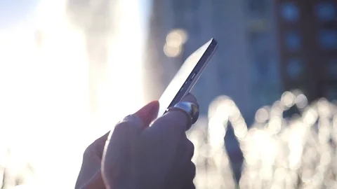 Holding a touch phone, flipping the screen, on a background of a fountain in the Stock Footage 76340398