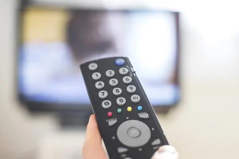 Holding a TV remote control in the hand, foreground, tv in the blurry Stock Photos