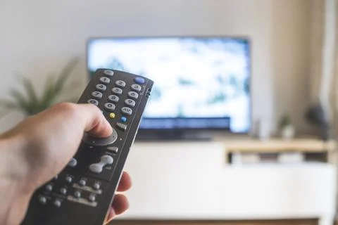 Holding a TV remote control in the hand, foreground, tv in the blurry Stock Photos
