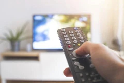 Holding a TV remote control in the hand, foreground, tv in the blurry 库存照片
