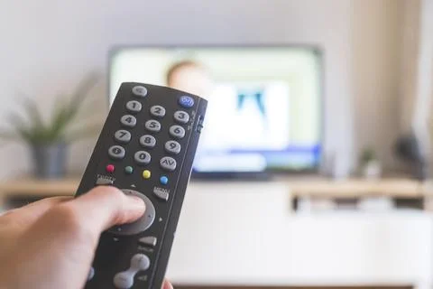 Holding a TV remote control in the hand, foreground, tv in the blurry Stock Photos