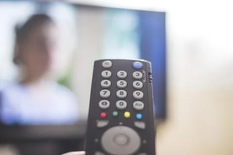 Holding a TV remote control in the hand, foreground, tv in the blurry Stock Photos