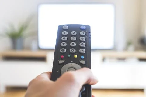Holding a TV remote control in the hand, foreground, tv in the blurry Stock Photos