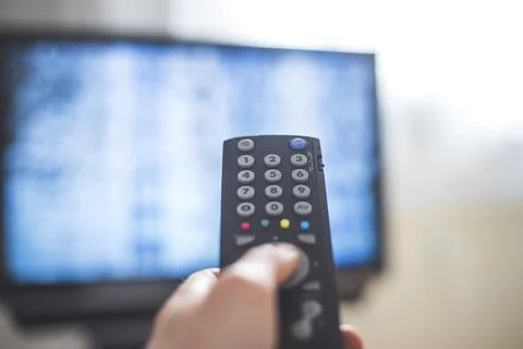 Holding a TV remote control in the hand, foreground, tv in the blurry Stock Photos