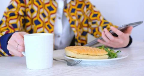 Holding white mug scrolling tablet wearing printed jacket at cafe table with Stock Photos