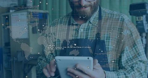 Holding white tablet, tech in plaid shirt and apron reviewing screen in workshop Stock Photos