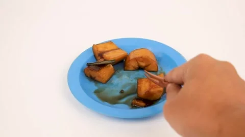 Holds a fork and picks up a piece of caramelized cassava snack from the plate. Vídeos de archivo 340487499