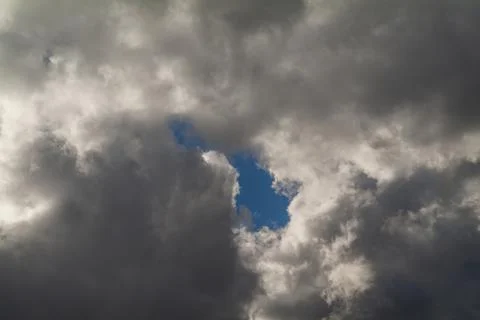 A hole in the dark clouds show a portion of blue sky Stock Photos
