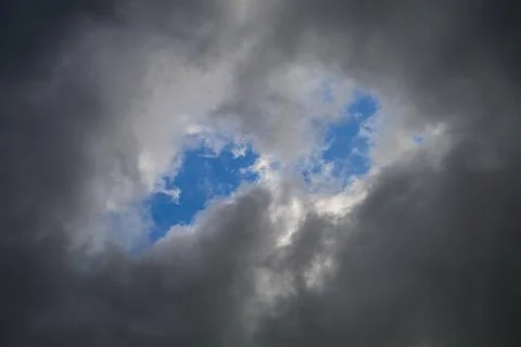 A hole in the dark clouds show a portion of blue sky Stock Photos