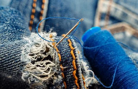 Hole in jeans. Needle with thread for darning jeans. Tools for work 스톡 사진