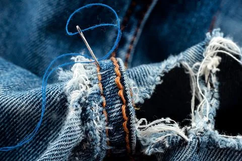 Hole in jeans. Needle with thread for darning jeans. Tools for work Foto stock