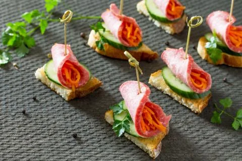 Holiday appetizer: Canapes on crispy bread with cucumber, carrots and sausage. Stock Photos