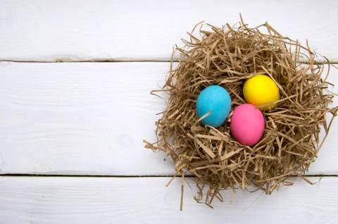 Holiday colored easter eggs in nest on white wooden table top view Stock Photos