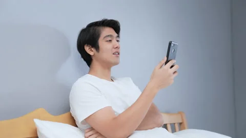 Holiday concept of 4k Resolution. Young Asian man playing mobile phone in bed Stock Footage 169818824