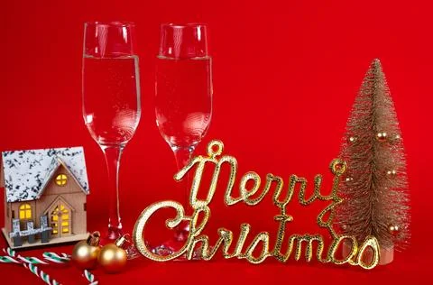Holiday flat-lay on red background with champagne flutes, mini tree and Merry Stock Photos