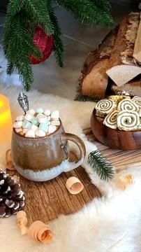 Holiday scene with rustic setup of steaming cocoa topped by marshmallows, candle Stock Photos
