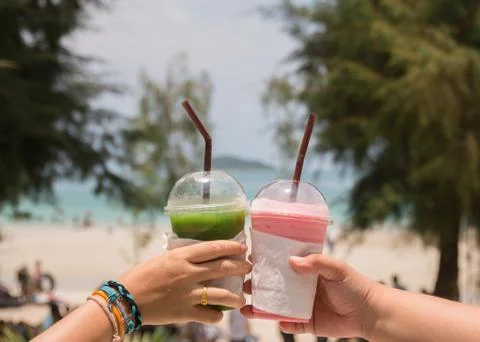 On holiday two women clinking their smoothie on beach at Thailand. Clinking c Stock Photos