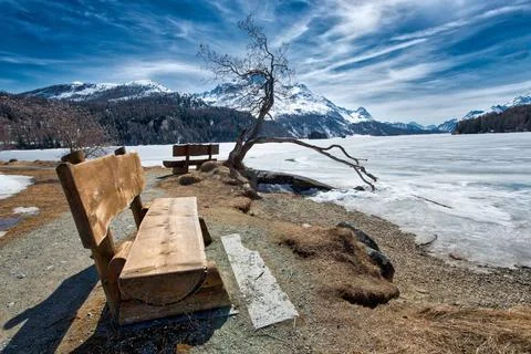Holzbank zum Bewundern der Landschaft auf dem Eis eines alpinen Sees bei S... Stock Photos