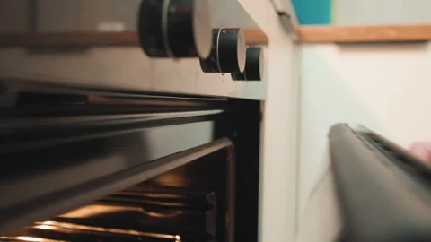 Home baker hand pulls oven handle to check baking, warm interior glow, gentle Stock Footage 337460649
