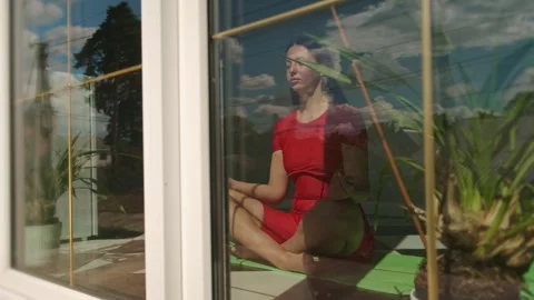 Home-based realistic meditation session with woman in red dress seated on yoga Stock Footage 309661608