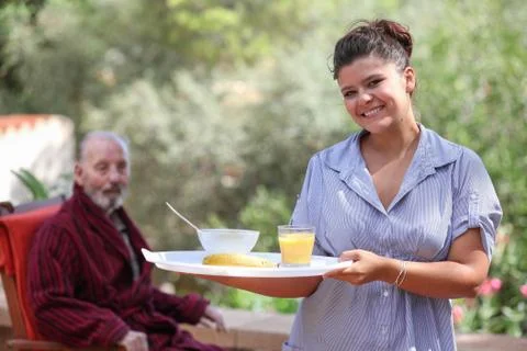 Home carer serving meal to elderly man Stock Photos