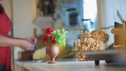 Home chef arranges flowers inside bright kitchen. Brightly lit kitchen with Stock Footage 347348864