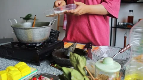 Home cook adding dry spice powders and condiments to cooking pot to season dish Stock Footage 344910740