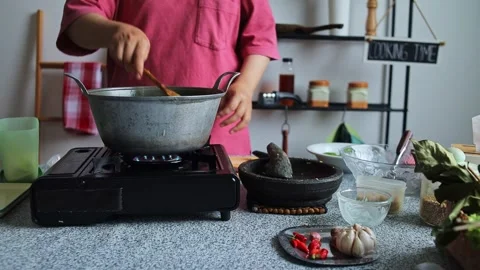 Home cook Adding granulated sugar with spoon simmering dish on portable burner Stock Footage 345379422