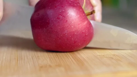 A home cook cuts a large red apple on a wooden board with a knife. Stock Footage 249697208