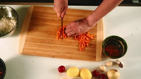 A home cook skillfully chops vibrant carrots and potatoes while preparing onions Vídeos de archivo 316635152