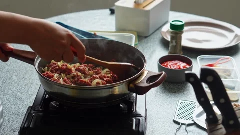 Home cook Stirring raw ground beef and sliced onions together in hot skillet Stock Footage 345376715
