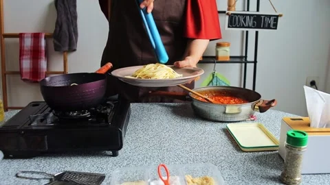 Home cook using blue kitchen tongs to lift cooked spaghetti from pot onto Stock Footage 345379528