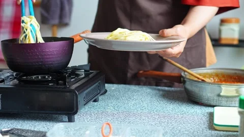 Home cook using blue tongs to transfer hot boiled spaghetti from pot onto plate Stock Footage 345379657