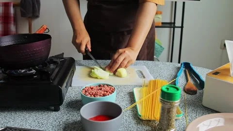 Home cook using sharp knife to slice yellow onion on plastic cutting board for Stock Footage 345379780