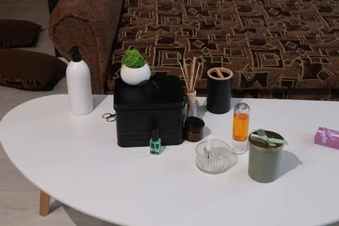 Home decor items arranged on a white coffee table with a patterned sofa in .. Stock Photos