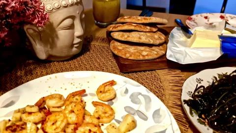 Home dining table with garlic shrimp, seaweed salad, crusty bread and butter Stock Footage 333323395