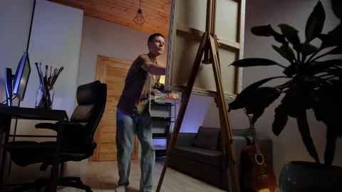 Home hobby in authentic interior man painting on canvas in cozy creative room Stock Footage 315433406