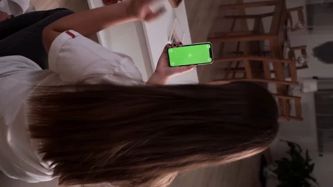 Home isolated. Back view of brunette holding chroma key green screen smartphone Video stock 128178052
