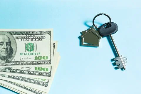 Home key with a keychain on a stack of $ 100 bills on a blue background. Purc Stock Photos
