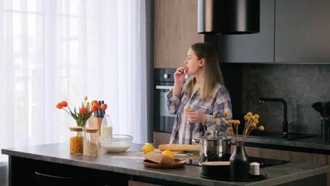 In home kitchen, woman happily eats freshly cut baguette. Housewife carefully Stock Footage 277399818