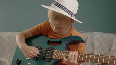Home Lesson Boy Kid Playing The Guitar. boy in white hat plays guitar at home. c Stock Footage 158856652