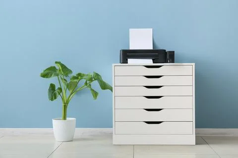 Home office printer and storage cabinet with green plant against blue wall, m Stock Photos