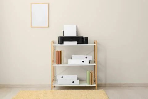 Home office printer and storage shelf with books and binders on light wall ba Stock Photos